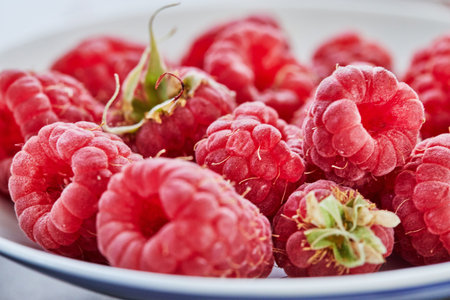 Fresh raspberries lying on white plate close-up shooting selective focus.