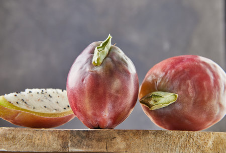 Peruvian apple cactus fruits whole and cut on wooden stand on gray board. Scientific name Cereus...