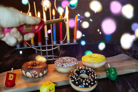 Happy Hanukkah and Hanukkah Sameach - traditional Jewish candlestick with candles, donuts and spinning tops on brown wooden background. Inscription in Hebrew with letters of the alphabet Nun, Pei. gimel, hey.の写真素材