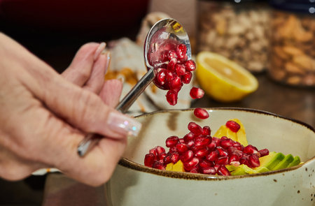Chef adds pomegranate seeds to a fruit salad at home in the kitchen