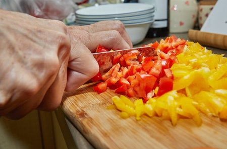 Woman cuts red and yellow bell peppers for cooking at home using recipe from the Internet. Preparation of ingredients and vegetables before cooking.の写真素材