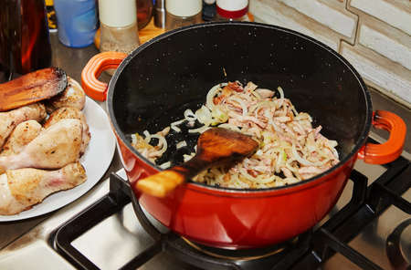Onions are fried in saucepan for cooking chicken legsの写真素材