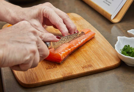 Chef cuts salmon with knife to prepare recipeの写真素材