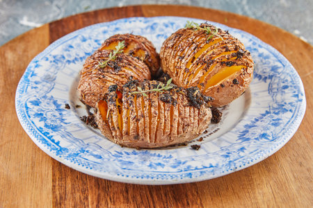 Oven baked potatoes Hasselback Hedgehog with Provence herbs on plate. French gourmet cuisine.