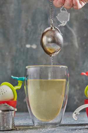 Brews tea in transparent glass with boiling water and tea strainer.