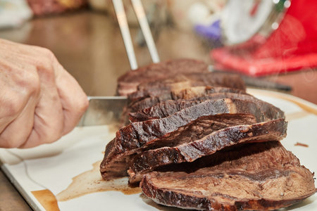 Chef cuts piece of beef fried with onions in wine sauce into slices for serving. French gourmet...