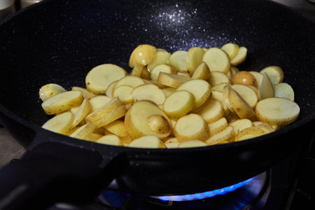 Sliced potatoes are fried in frying pan on gas stoveの写真素材