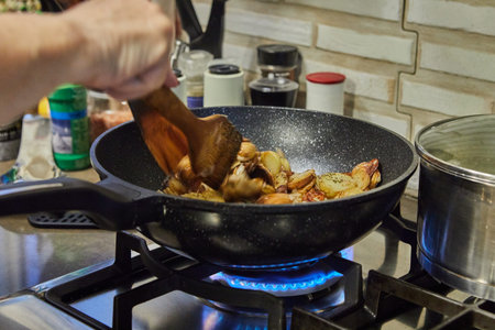 Chef stirs Sliced potatoes with mushrooms infrying pan on gas stoveの写真素材