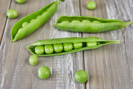 Opened pods of fresh green peas on wooden background.の写真素材