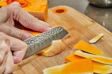 Chef cuts pumpkin in the shape of pear on wooden board in the home kitchen.