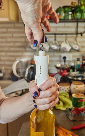 Woman opens bottle of white wine with special corkscrew