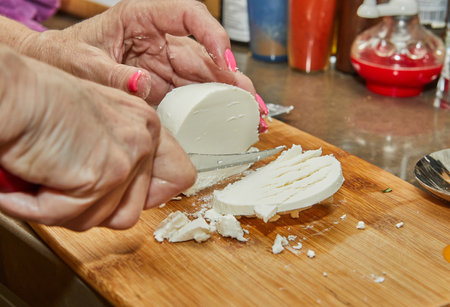 Chef cuts the cheese with knife on wooden board for making a pie.の写真素材