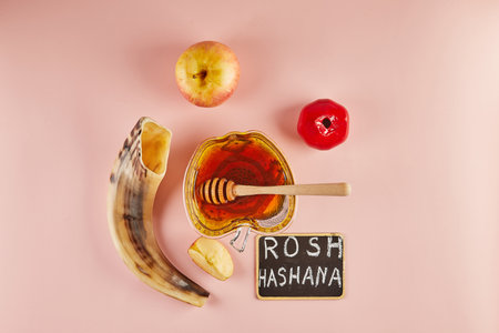 Rosh hashanah lettering - jewish new year holiday concept. Bowl in the shape of an apple with honey, apples, pomegranates, shofar on pink background.の写真素材