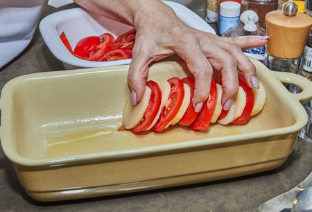 Chef puts tomatoes, potatoes and onions cut into circles in ceramic dishの写真素材