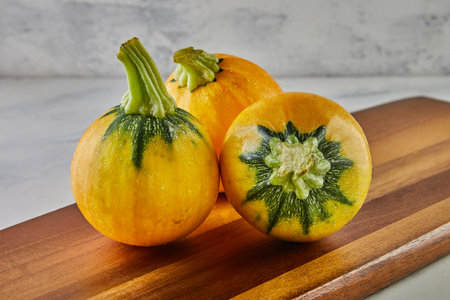 Round yellow and green zucchini on wooden board on gray background.の写真素材