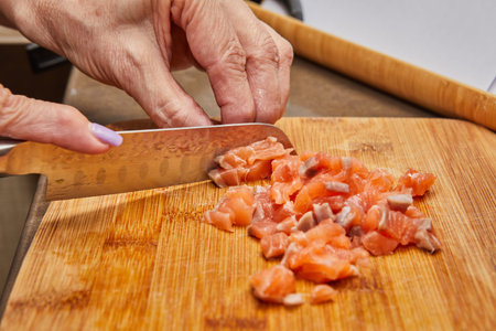 A skilled chefs hands carefully cutting a piece of fresh salmon using a sharp knife on a wooden cutting board in a well-equipped kitchen.の写真素材