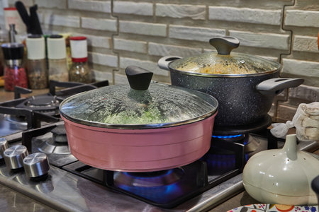 Close-up of fresh zucchini slices sizzling in a hot skillet on a gas stove, with flames licking the...