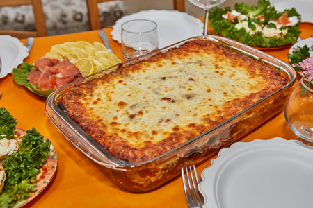 Beautifully decorated dining table for a festive New Year's Eve celebration with delicious lasagna, salmon garnished with fresh herbs and elegant tableware.の写真素材