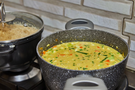 A professional chef wearing a white uniform is preparing a delicious and healthy couscous soup with fresh green vegetables on a stainless steel gas stove, creating a mouthwatering and nutritious dish.の写真素材