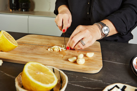 A woman, a housewife, cuts garlic in a stylish modern kitchen with a marble background. She prepares...
