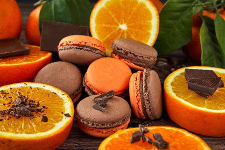 Delicious chocolate-flavored macaroons with orange on a dark wooden background and green leaves. Ideal image for pastries, desserts or food blog content.の写真素材
