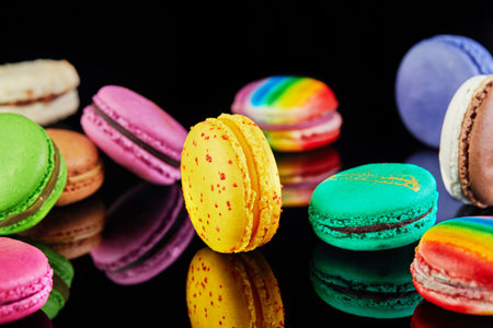 Vibrant and colorful assortment of macarons artfully arranged on a pristine black surface, creating an enticing display of reflections.の写真素材