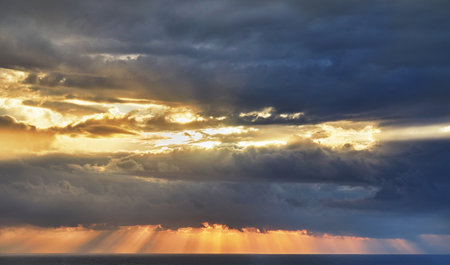 Dramatic thunderclouds over mediterranean sea with sun rays breaking throughの写真素材