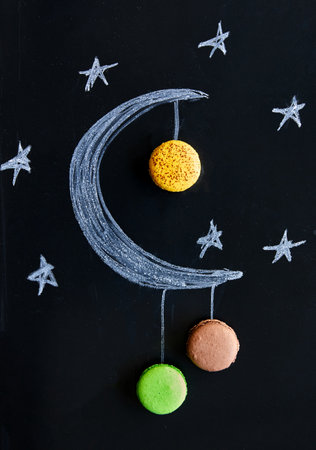 Chalk drawing of a crescent moon with macarons hanging from itの写真素材