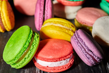 Assorted colorful French macarons on black wooden table. Pink, green, yellow, blue colors. Flavors chocolate, vanilla, strawberry. Isolated on black background, perfect for photos.の写真素材