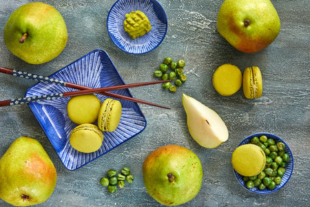 Green matcha macarons with sliced ripe pears on a blue plate, set on a stone table. Represents a healthy lifestyle with organic desserts. Close-up view showcases the delicious presentation.の写真素材