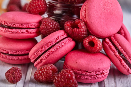 A stack of pink macarons with raspberries on a wooden table, showcasing a delicious dessert made...