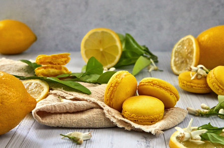 Delicious lemon flavored macaron on a light background with green lemon tree leaves and flowers. Ideal image for pastries, desserts or food blog content.の写真素材