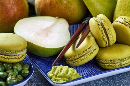 Green matcha macarons with sliced ripe pears on a blue plate, set on a stone table. Represents a healthy lifestyle with organic desserts. Close-up view showcases the delicious presentation.の写真素材