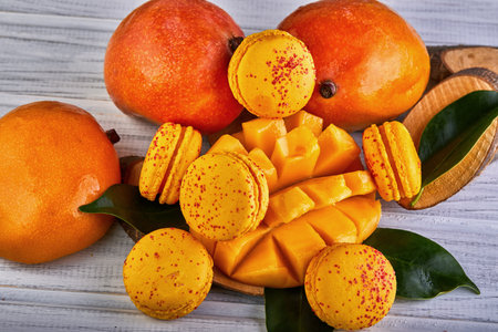 A variety of mangoes and macarons are displayed on a table, showing a colorful array of natural foods. The combination of fruits and sweets highlights the diverse range of ingredients in cuisineの写真素材