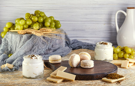 A wooden cutting board showcasing a variety of food items including macarons, chocolate, yogurt, and grapes. The display features a mix of sweet and savory ingredients on natural materialの写真素材