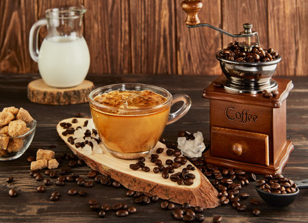 Coffee with milk in glass cup, vintage coffee grinder and jug with milk, lump sugar on wooden background.の写真素材