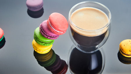 A cup of coffee sits on the table, accompanied by a variety of colorful macarons. The food and drinkware create a delightful display of ingredients in this cuisineの写真素材