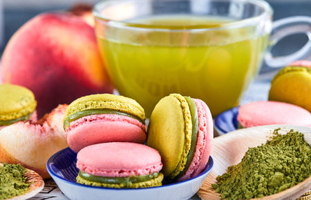 A delightful pairing of a bowl of colorful macarons next to a cup of antioxidant rich green tea, creating a perfect balance of indulgence and refreshment on the tableの写真素材