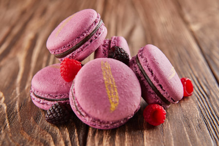 A delightful pile of purple macarons with chocolate and berries arranged on a wooden table, showing the perfect combination of sweet ingredients and baked goodsの写真素材