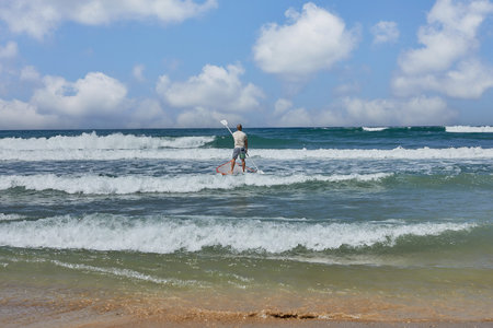 A person is gliding on a surfboard in the fluid water of the ocean, under a cloudy sky, with the...