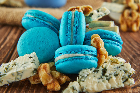 A wooden table adorned with a colorful array of macarons, nuts, and cheese. The vibrant mix of food items creates a stunning display of colors, from electric blue to azure and greenの写真素材