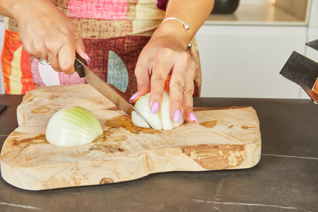 A woman chops onions on a wooden board in her home kitchen.の写真素材