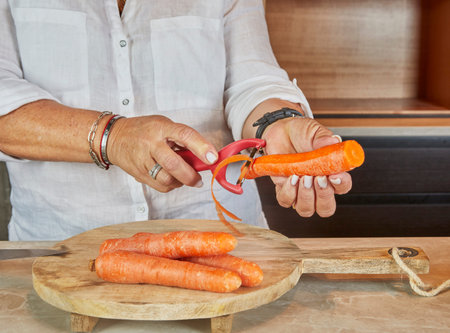 Woman Peeling Carrots in Home Kitchen Preparing Fresh Vegetables.