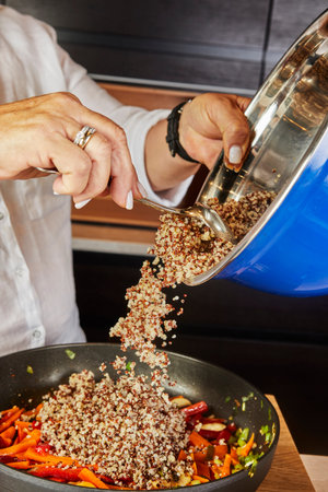 A Woman Throws Quinoa from a Bowl into a Frying Pan on an Electric Stove.の写真素材