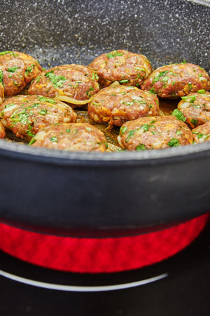 Frying pan with meat cutlets with seasonings on an electric stove in a home kitchen. Close-up.