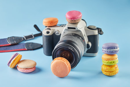 Colorful macarons of different flavors with a film camera on a blue background with shadow.