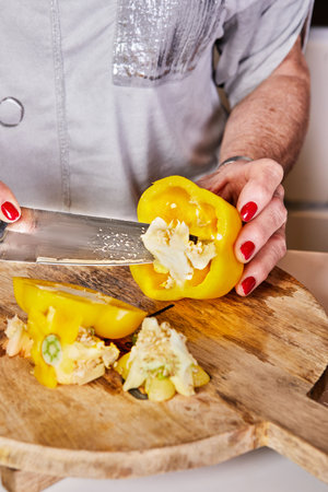 Close-up of hands slicing a yellow bell pepper on a wooden cutting board, showcasing cooking preparation and fresh ingredients.の写真素材