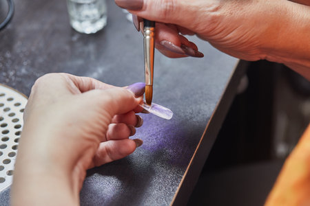 Close-up of a nail technician using a brush to apply gel to a nail in a salon setting.の写真素材