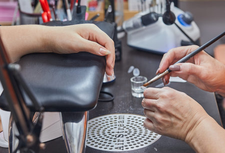 Close-up of a nail technician using a brush to apply gel to a nail in a salon setting.の写真素材
