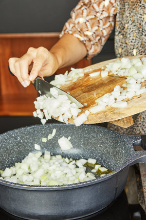Chopped onions being transferred from a wooden board into a frying pan with oil for sauting.の写真素材